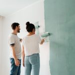A couple collaborates to paint a wall with a roller indoors, showcasing teamwork. — Outdoor Flooring Ideas