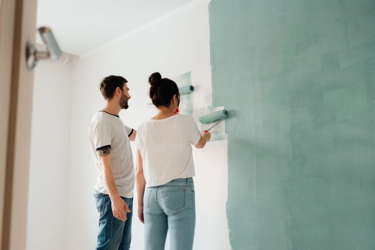 A couple collaborates to paint a wall with a roller indoors, showcasing teamwork. — Outdoor Flooring Ideas