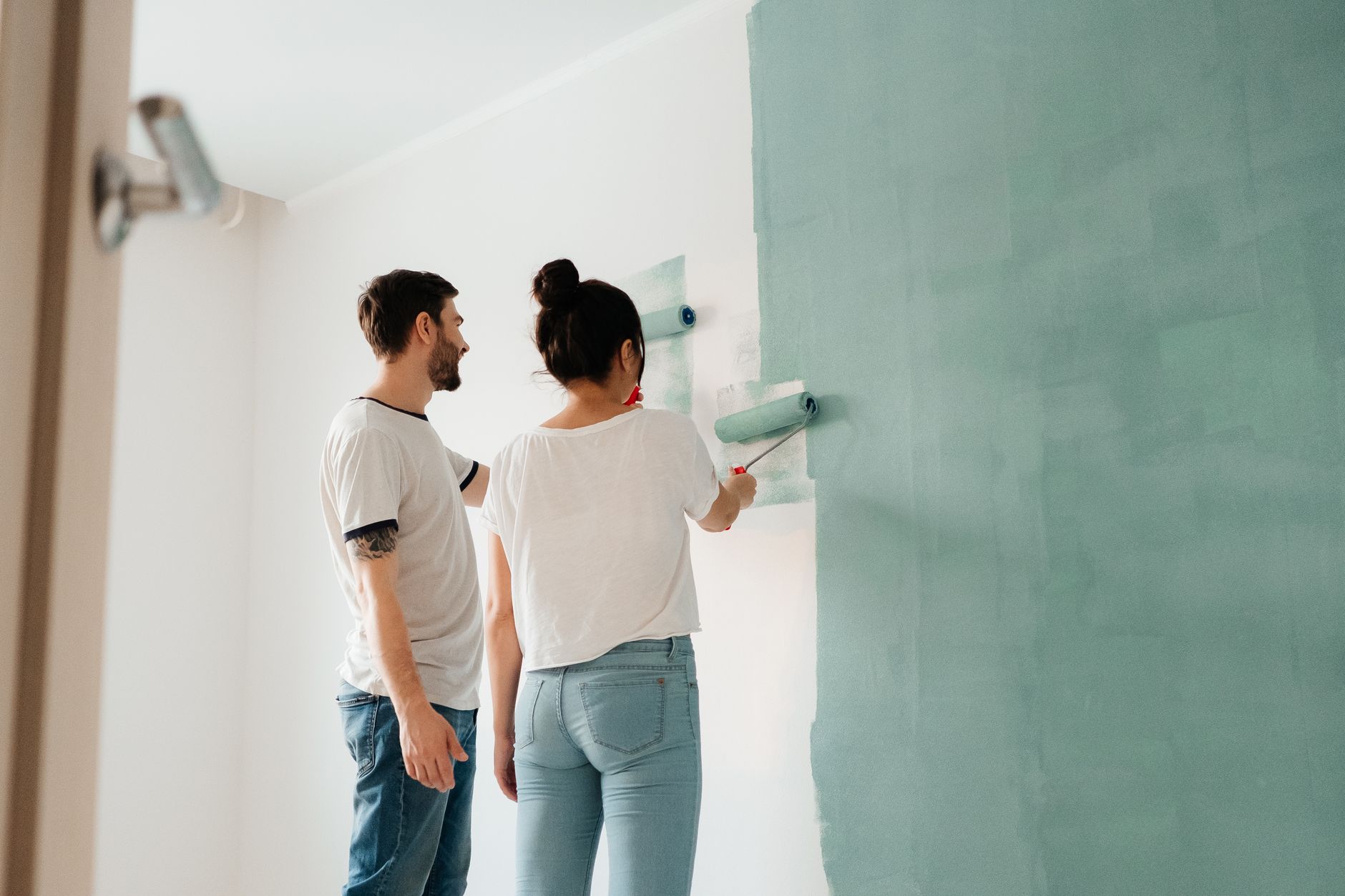 A couple collaborates to paint a wall with a roller indoors, showcasing teamwork. — Outdoor Flooring Ideas