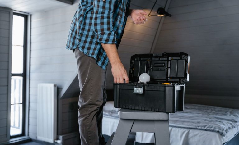 Person in plaid shirt fixing a light bulb using a toolbox in a rustic attic interior. — Parasols and buyer guide to their acc