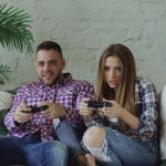 Young couple playing video games intensely on a couch, enjoying leisure time indoors. — Planning to access online slot games-