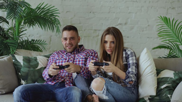 Young couple playing video games intensely on a couch, enjoying leisure time indoors. — Planning to access online slot games-