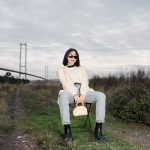 Stylish woman in sunglasses sitting by a bridge, showcasing modern fashion against a natural backdrop. — Raw Cannabis Delight
