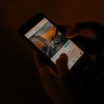 Hands holding a smartphone browsing social media in low light. — Save Time and Resources by Leveraging a Facebook Ads Agency