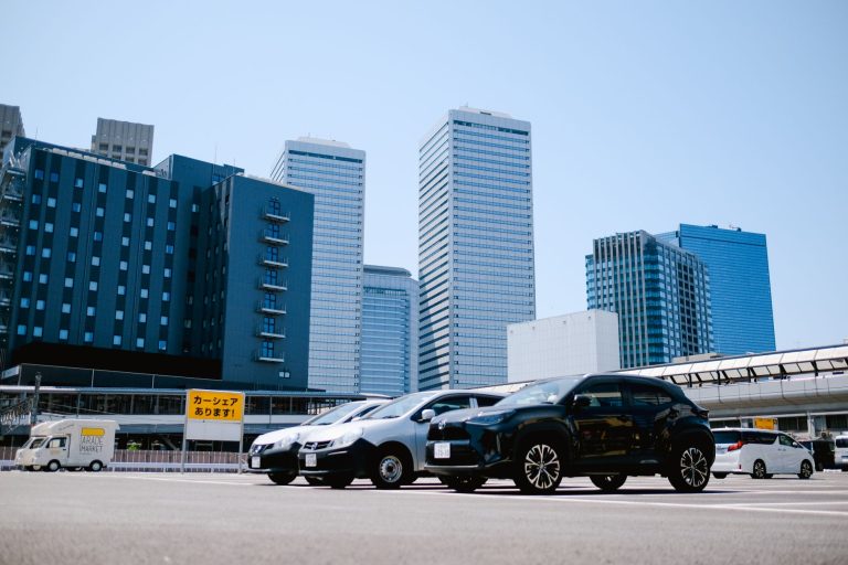 City parking lot with modern buildings and parked cars under a clear sky. — Ship A Car Ensures Safe and Reliable Rochester Ca