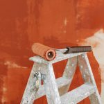 Paint roller on a ladder with a partially painted red wall in the background. — Simple method to cover chair