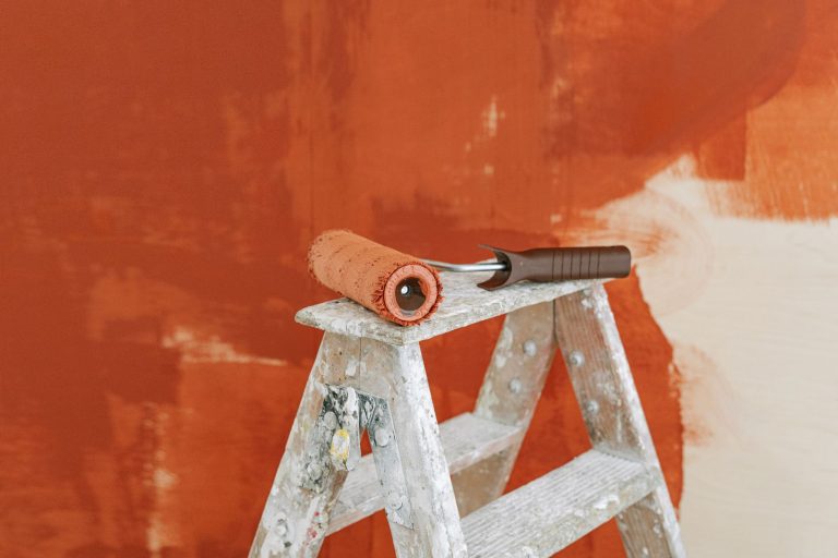 Paint roller on a ladder with a partially painted red wall in the background. — Simple method to cover chair