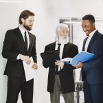 Three businessmen in suits discussing documents in a modern office setting, showcasing teamwork. — Steps to Hunt for a Perfec