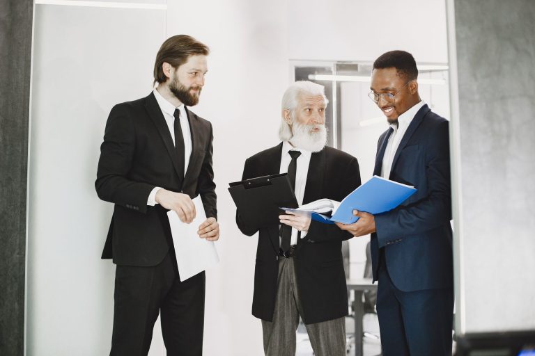 Three businessmen in suits discussing documents in a modern office setting, showcasing teamwork. — Steps to Hunt for a Perfec