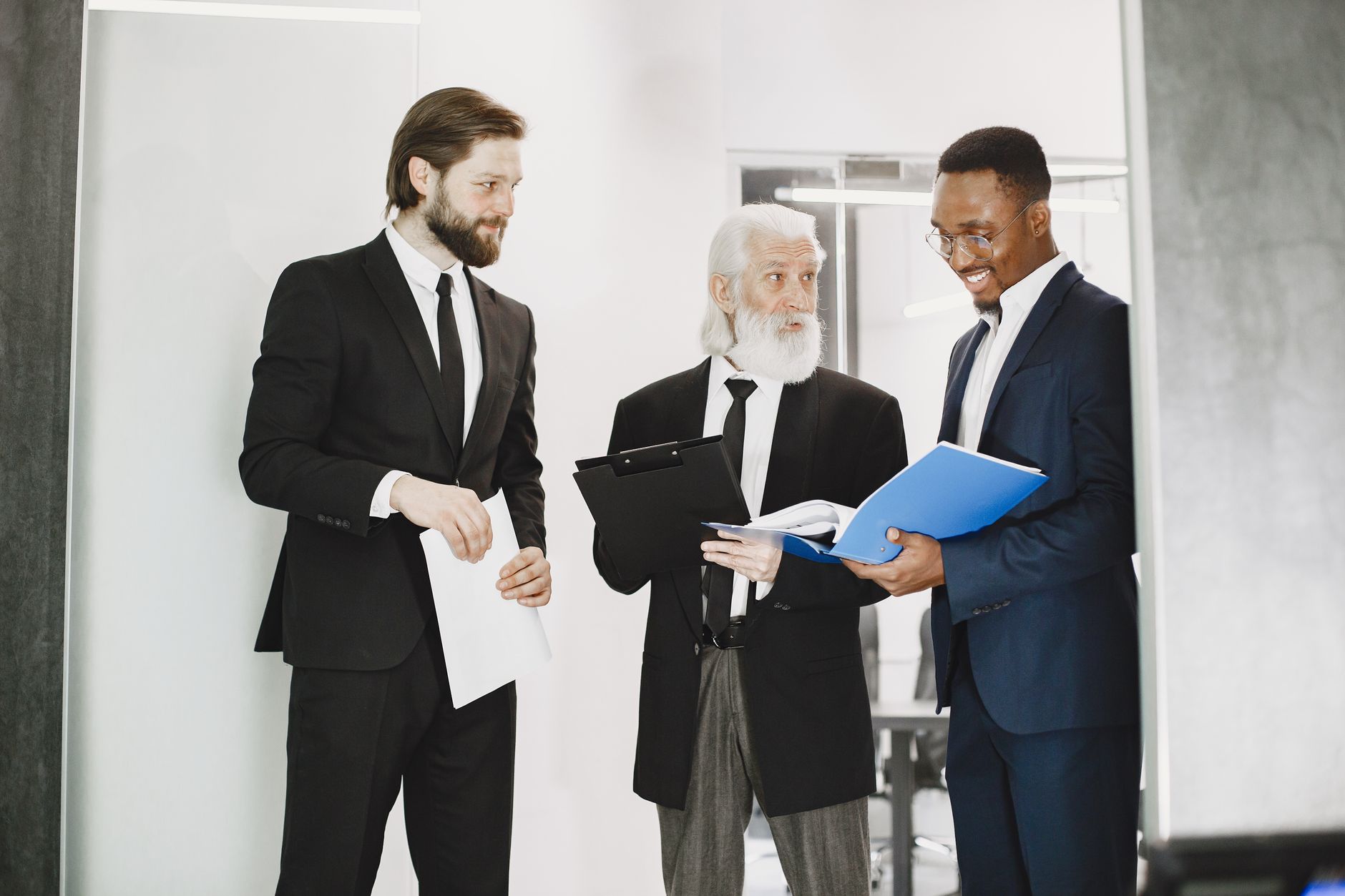 Three businessmen in suits discussing documents in a modern office setting, showcasing teamwork. — Steps to Hunt for a Perfec