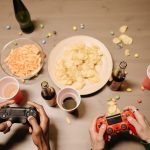Two gamers playing video games with snacks and drinks on table, a perfect setup for gaming night. — Take Advantage of Generou