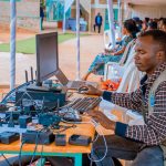 Technician managing electrical and computer setup at an outdoor event with attentive audience. — The Biggest Social Media Mar