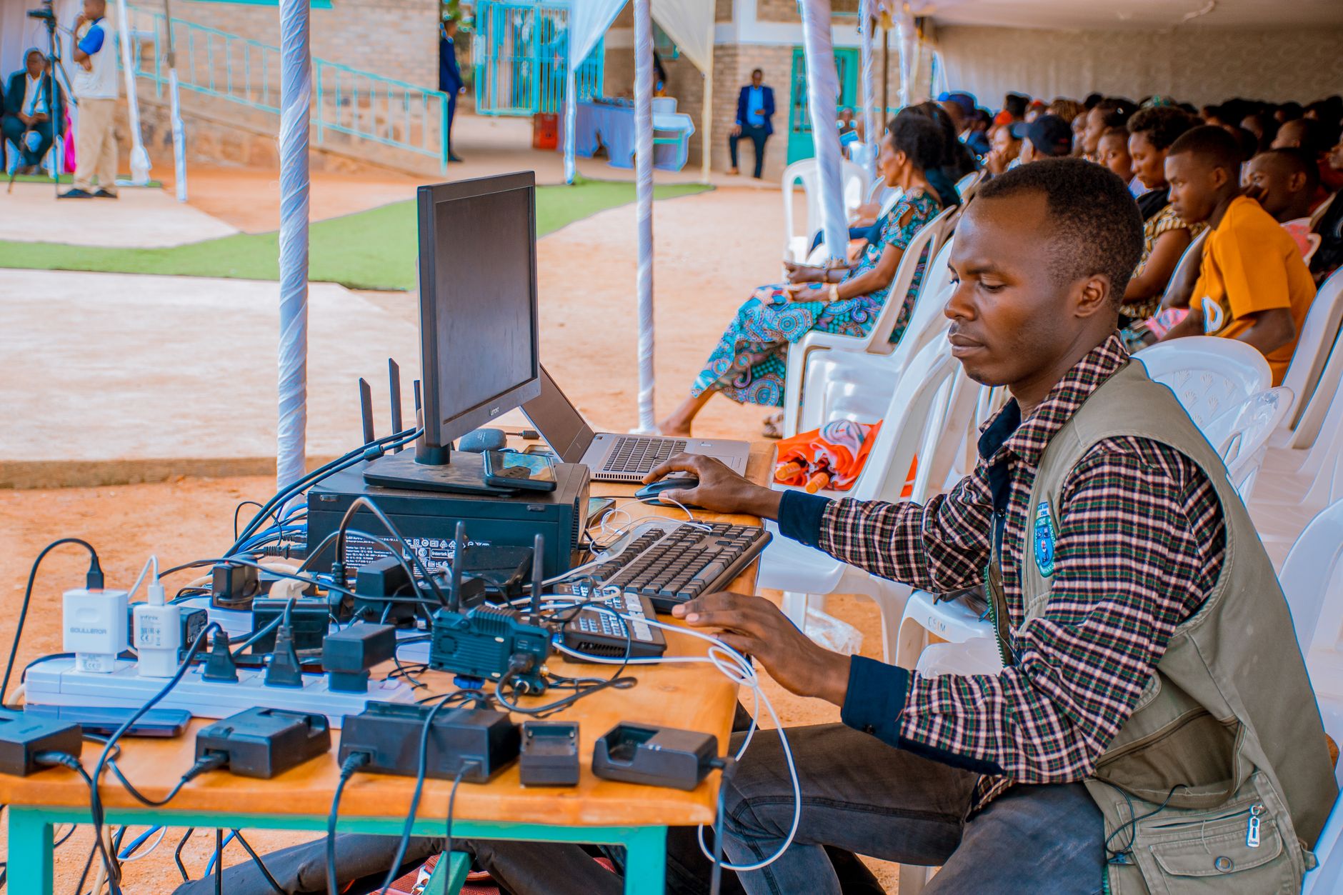 Technician managing electrical and computer setup at an outdoor event with attentive audience. — The Biggest Social Media Mar