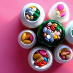 Top view of various medication pills and capsules in containers with bright pink backdrop. — The Cost of Testosterone Therapy