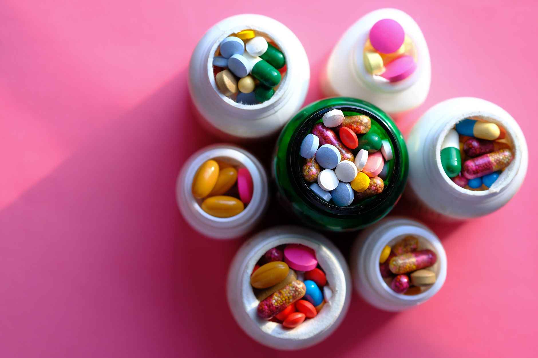 Top view of various medication pills and capsules in containers with bright pink backdrop. — The Cost of Testosterone Therapy