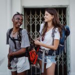Two young women backpacking and smiling in a lively urban setting, ideal for travel-focused content. — The General Hiring Sol