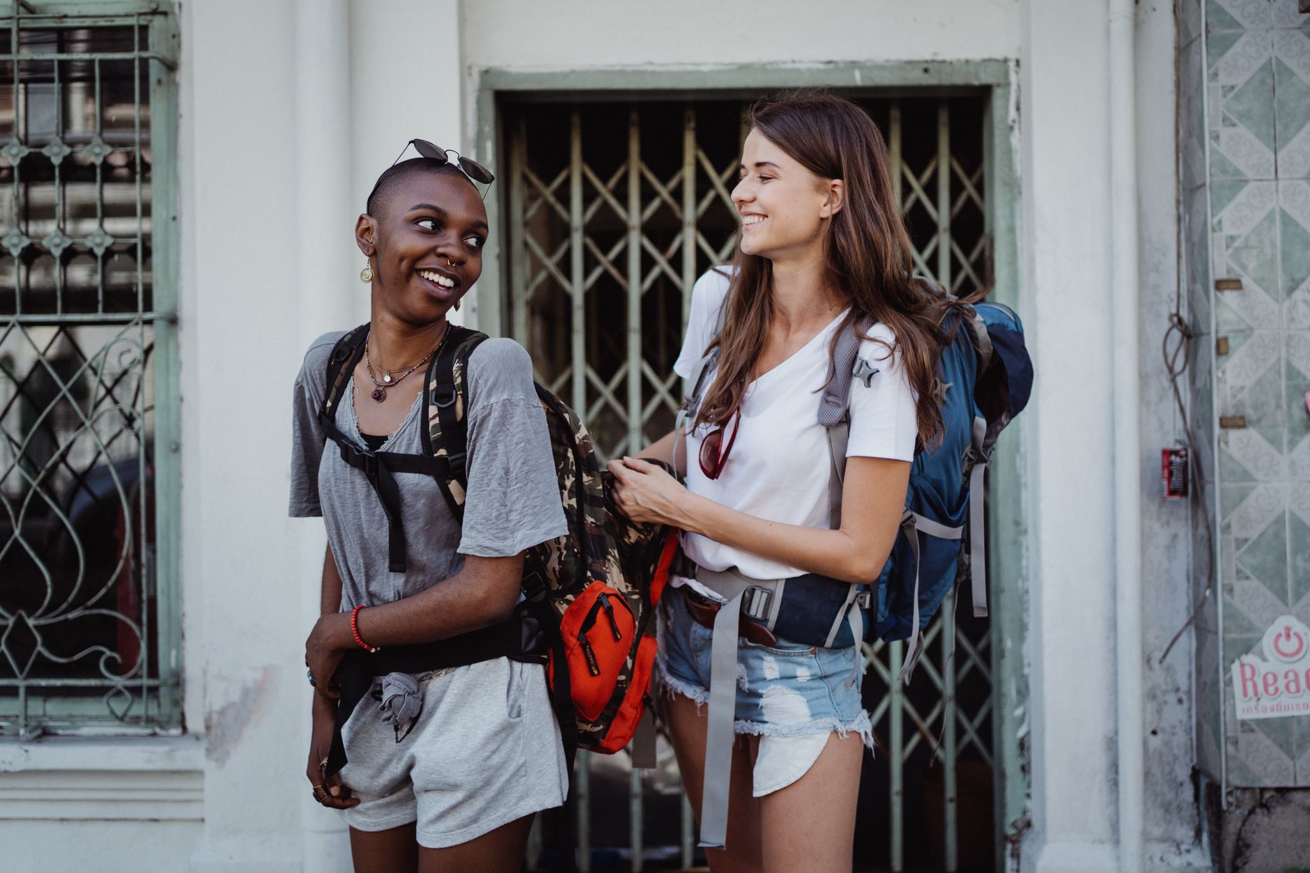 Two young women backpacking and smiling in a lively urban setting, ideal for travel-focused content. — The General Hiring Sol