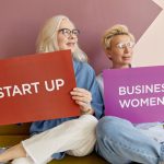 Two women on a sofa holding signs promoting startup and business women. — The server is one of the most important things for