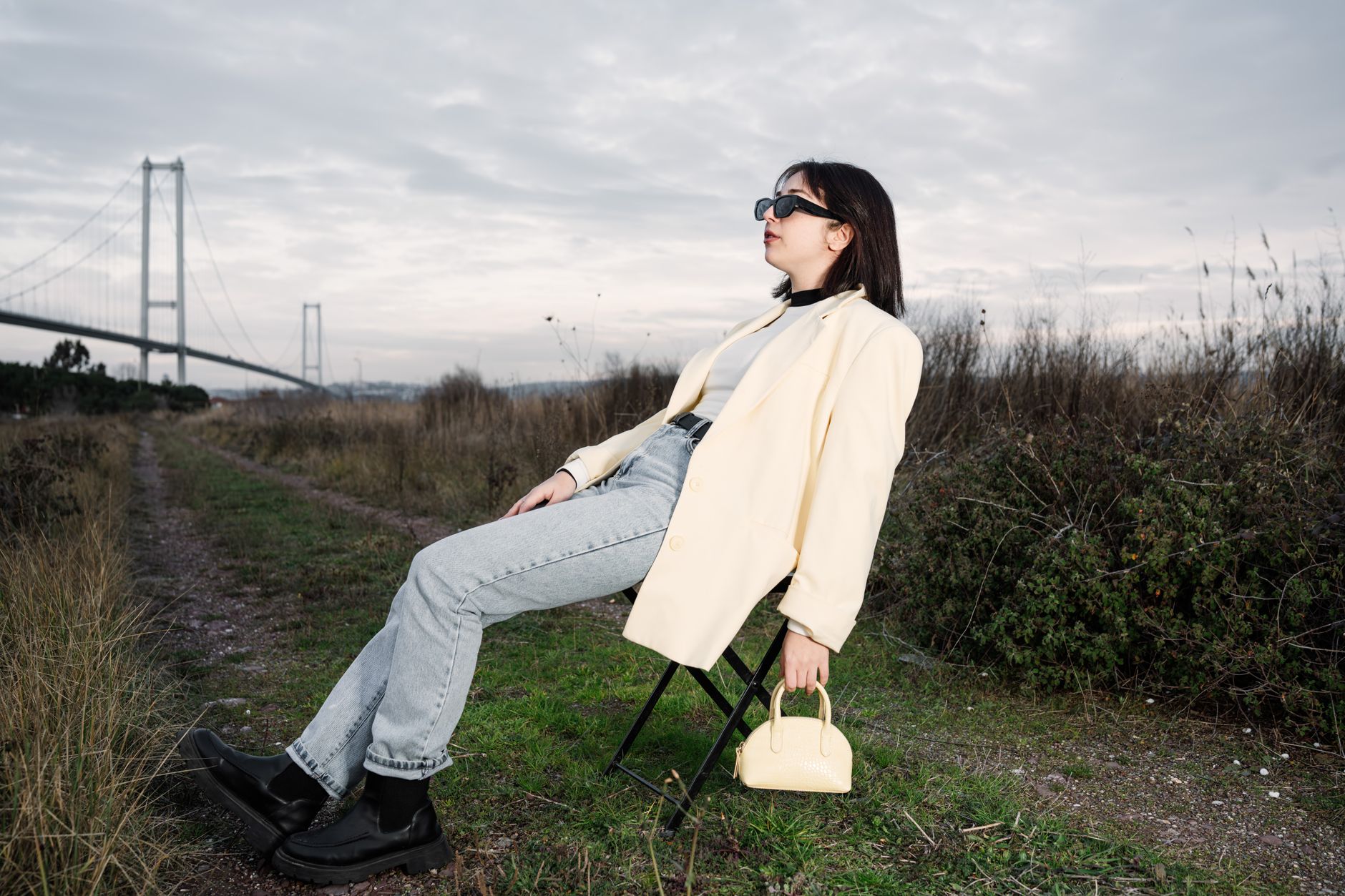 A stylish woman in sunglasses relaxes on a chair by a bridge in nature. — Tips on Maintaining and Cleaning a Weed Filter for