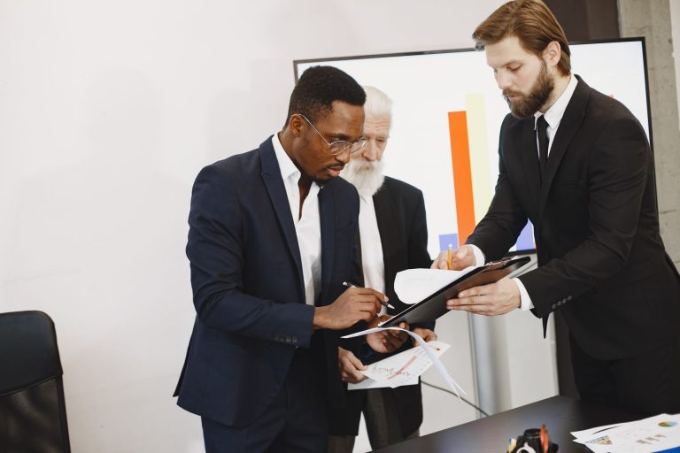 Three businessmen engaged in document signing in a modern office setting. — Top Loafers for Men