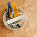 A collection of home renovation tools in a bucket on a wooden floor, ready for a painting project. — Understanding The Real M