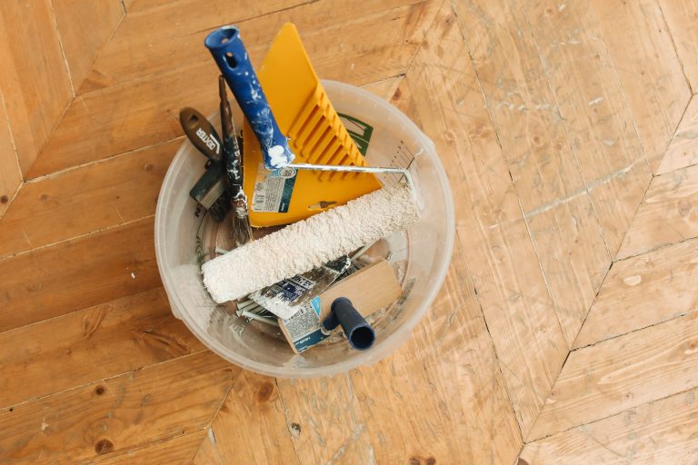 A collection of home renovation tools in a bucket on a wooden floor, ready for a painting project. — Understanding The Real M