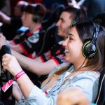 A group of people enjoying an immersive gaming experience at an e-sports center with headphones and steering wheels. — Use th