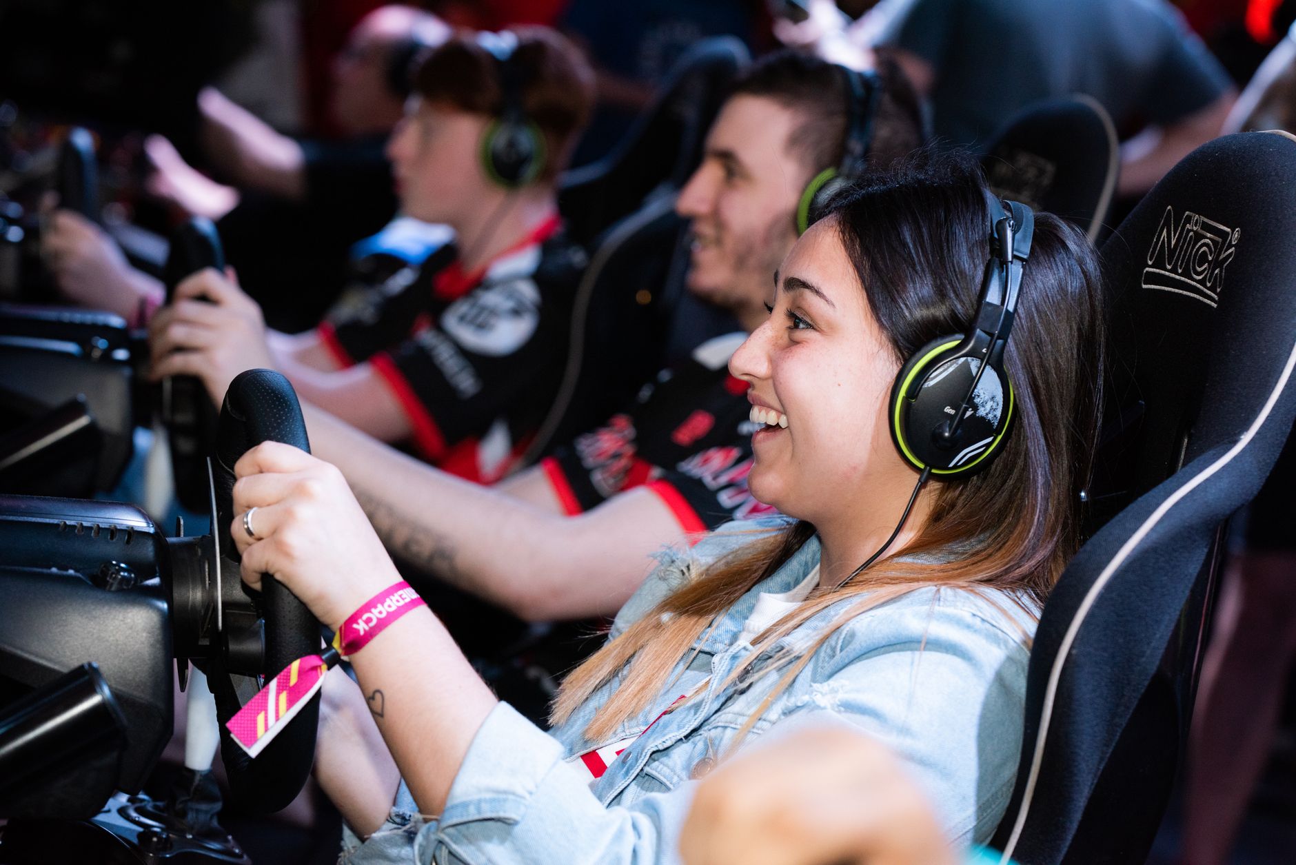 A group of people enjoying an immersive gaming experience at an e-sports center with headphones and steering wheels. — Use th