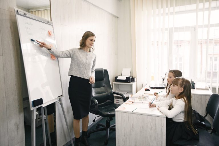 A female teacher guiding two girls during a lesson in a bright classroom with a whiteboard. — What are the various steps of s
