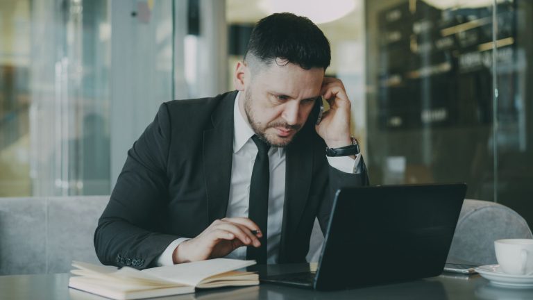 Focused businessman in suit multitasking on phone and laptop in modern office. — WHAT MEDICATIONS ARE PROVEN TO HELP PEOPLE Q
