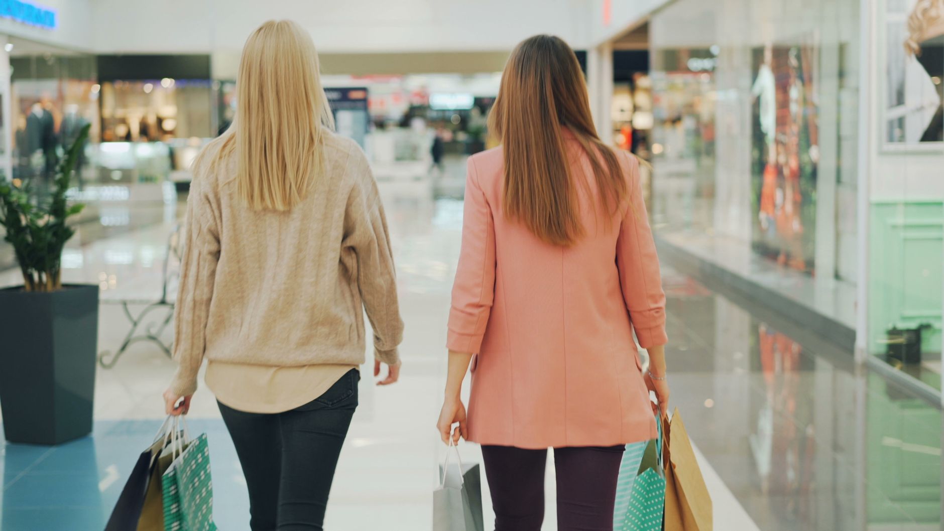 Two women walking in a mall holding shopping bags, back view. — What's the Best Way to Stay on Top of UK Hot Deals?
