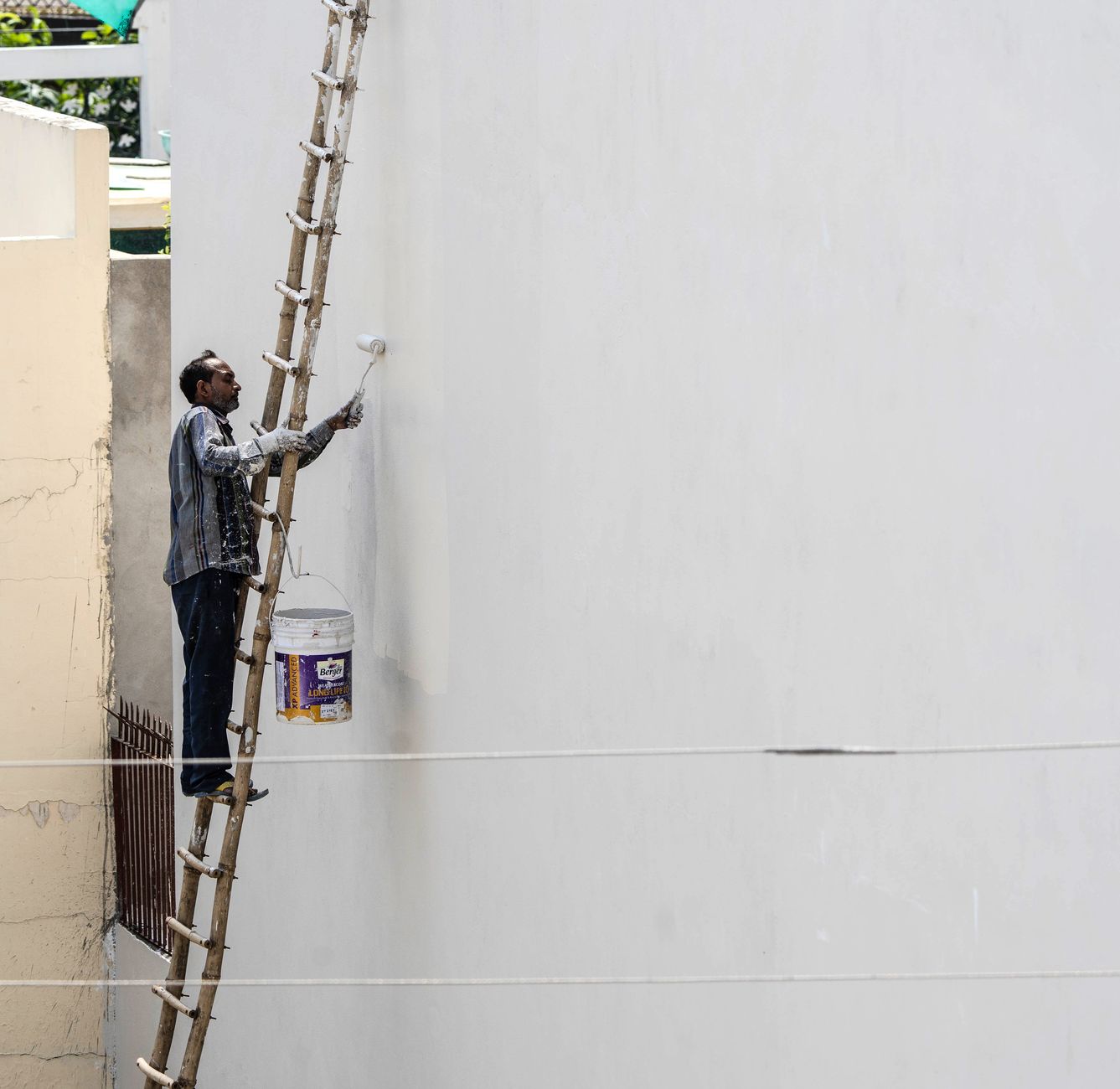 A man on a ladder painting a building's exterior wall with a roller brush outdoors. — Why Choose an eBay Transport Company fo