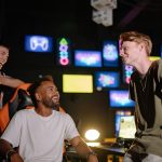 Three young men laughing and enjoying a gaming session in a vibrant room with multiple screens. — Why do people select soccer