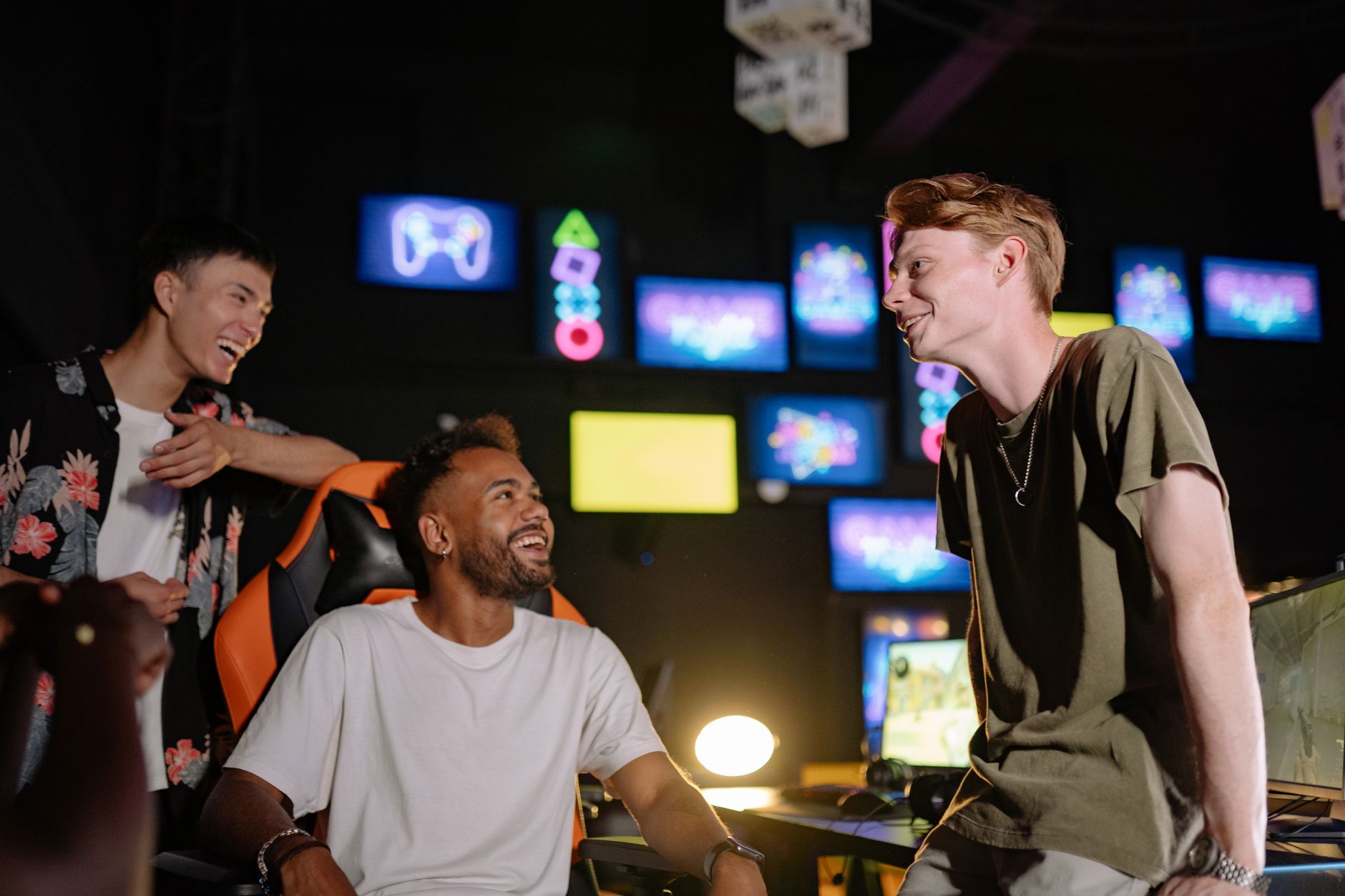Three young men laughing and enjoying a gaming session in a vibrant room with multiple screens. — Why do people select soccer