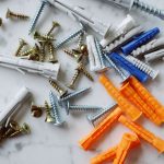 Set of various multicolored plastic dowels with assorted metal screws of different sizes placed on white marble table in mode