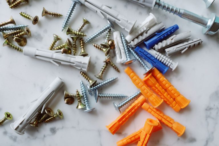 Set of various multicolored plastic dowels with assorted metal screws of different sizes placed on white marble table in mode