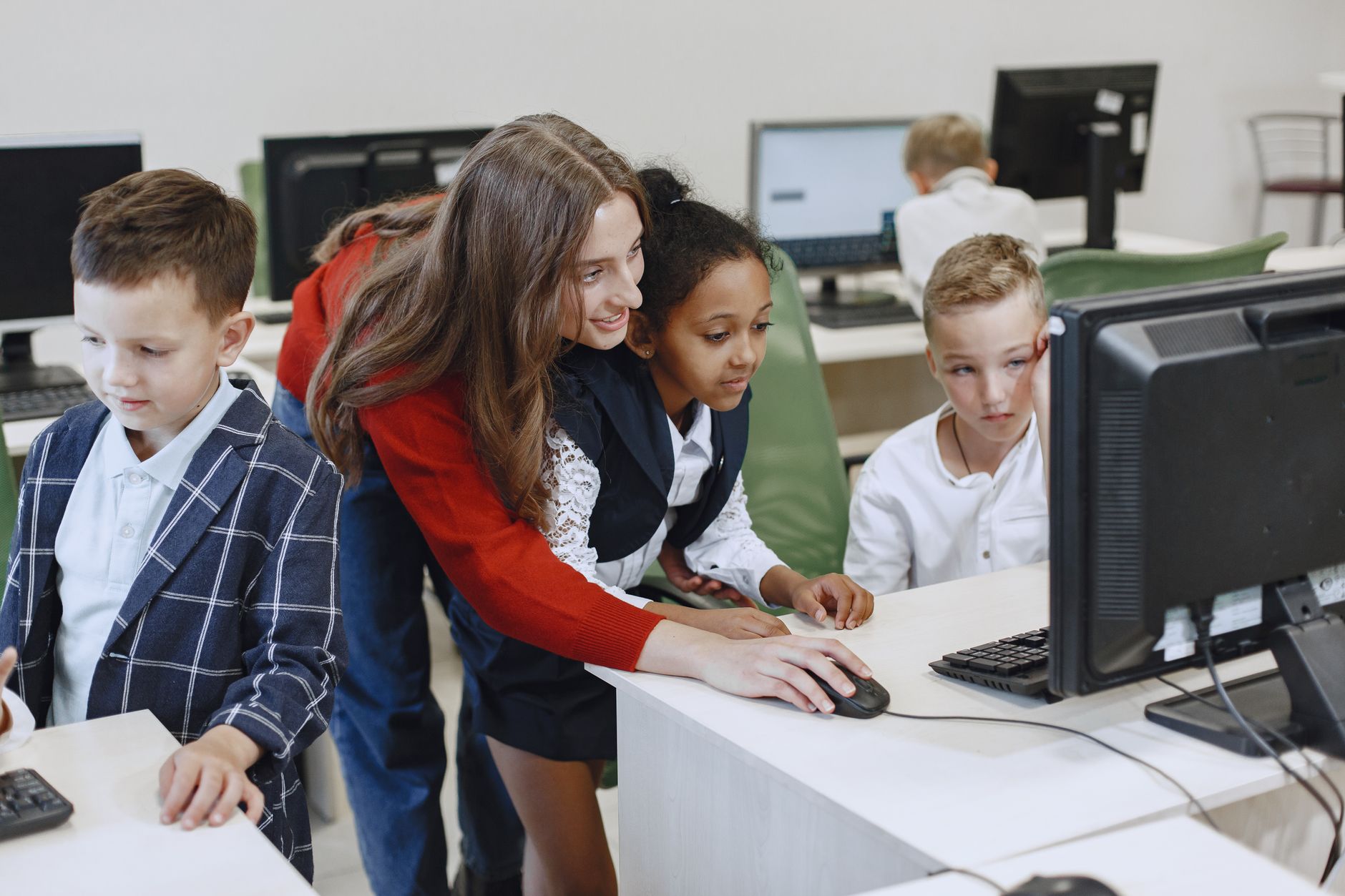 Teacher engaging with diverse children in a technology lesson using computers in a modern classroom. — Why Instruct Your Youn