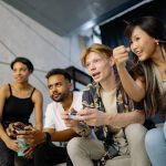 Four friends gaming enthusiastically inside a modern home, enjoying a lively moment. — Why Play The Online Lottery On Ligaz88