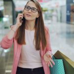 Woman in a mall with shopping bags, talking on phone, wearing pink blazer. — Why Should You Buy Things Online?