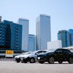 City parking lot with modern buildings and parked cars under a clear sky. — Why Should You Use a Cover Over Your Car?