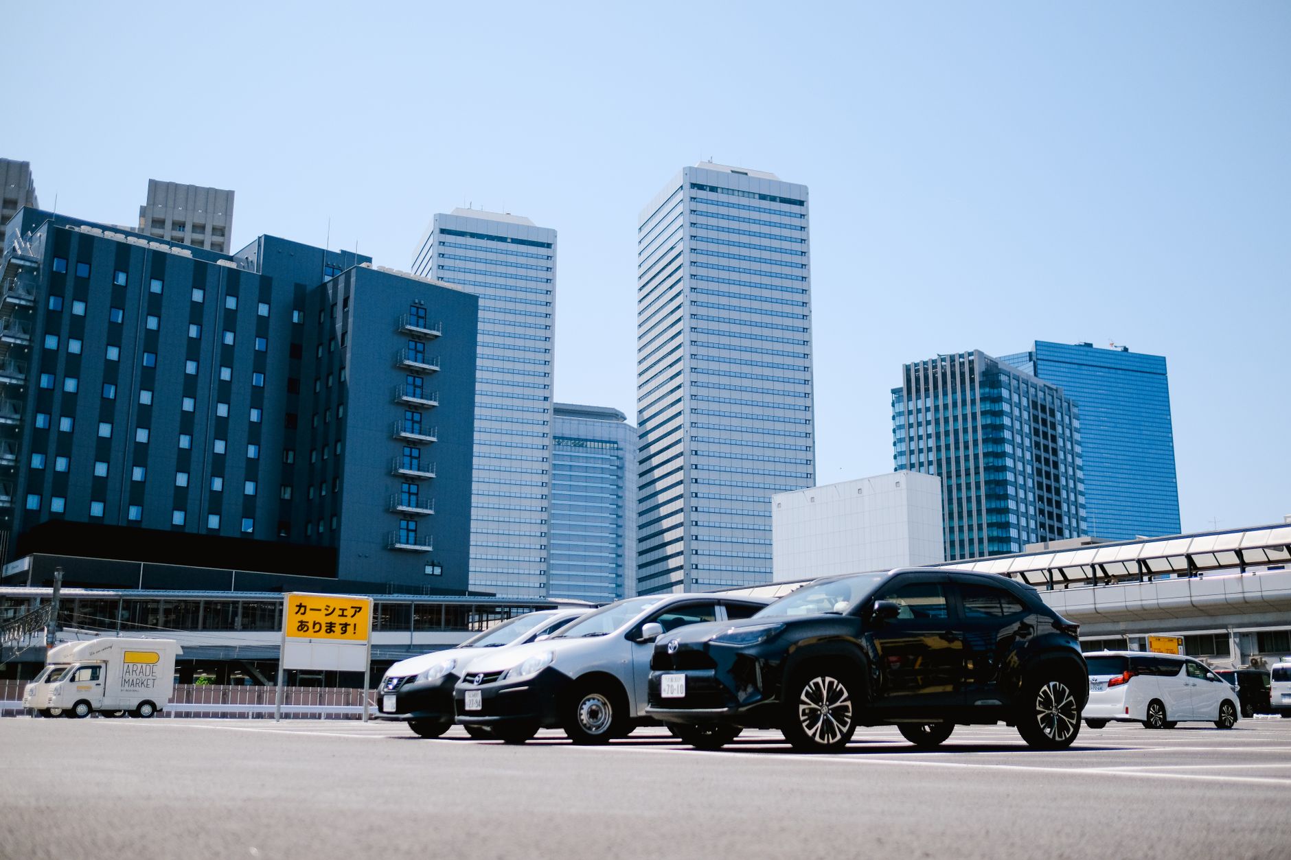 City parking lot with modern buildings and parked cars under a clear sky. — Why Should You Use a Cover Over Your Car?