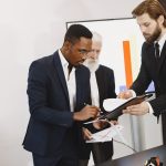 Three businessmen engaged in document signing in a modern office setting. — Work in Media Content Production at Fox on a Part